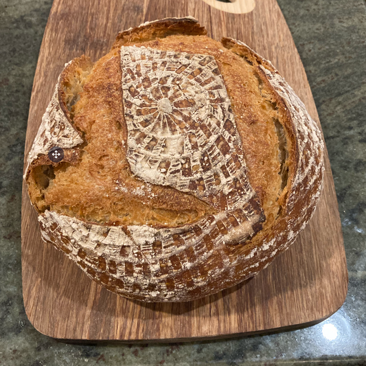 Loaf of bread on a wooden cutting board with a decorative cloth